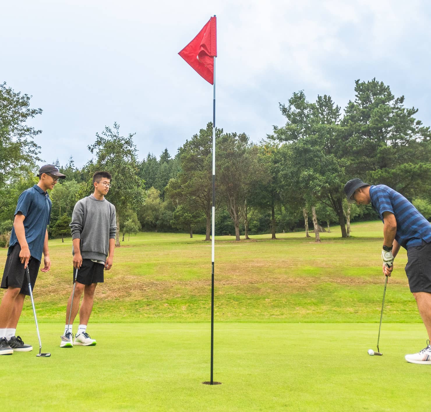 Two golfers watching as another prepares to putt into the hole at Sidmouth Golf Club
